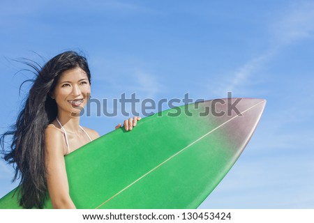 Beautiful young Asian Hawaiian woman surfer girl in bikini with surfboard standing on a beach with blue sky