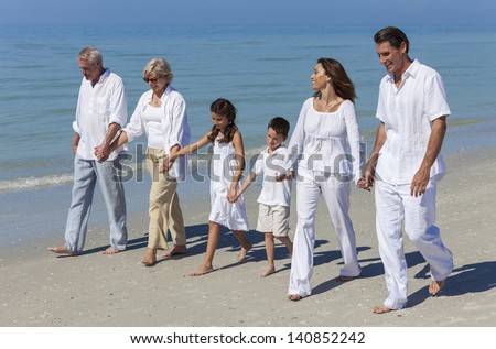A happy family of grandparents, mother, father and two children, son and daughter, walking holding hands and having fun in the sand of a sunny beach