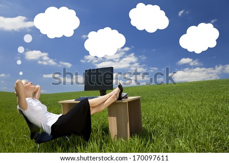 Business concept shot of a beautiful young woman relaxing at a desk in a green field day dreaming, white dream clouds in a blue sky.