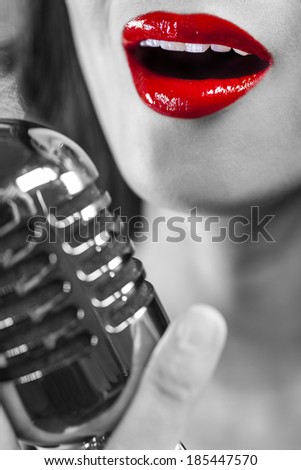 Black and white close up of beautiful female woman singer mouth with red lips singing into a vintage microphone in a night club