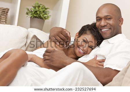 A happy African American man and woman romantic couple in their thirties cuddllng embracing at home.