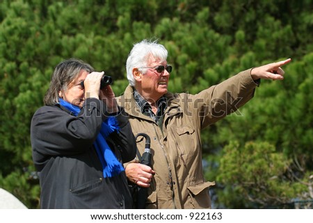 An elderly married couple sightseeing with binoculars