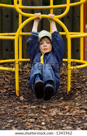 A young boy dressed up against the weather swinging on a climbing frame