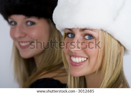 Two beautiful Russian women wearing fur hats, shot in three quarter profile, one in focus one out but both smiling for the camera