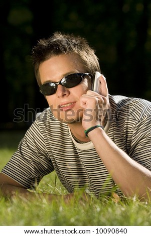 A fashionable young man chats on his mobile phone while laying down outside bathed in summer sunshine