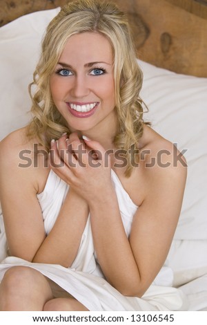 A beautiful young woman sits up in bed naked wrapped in a sheet and smiling excitedly