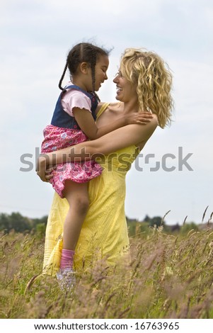 A beautiful blond haired blue eyed young woman having fun in a field of long grass with her mixed race young daughter