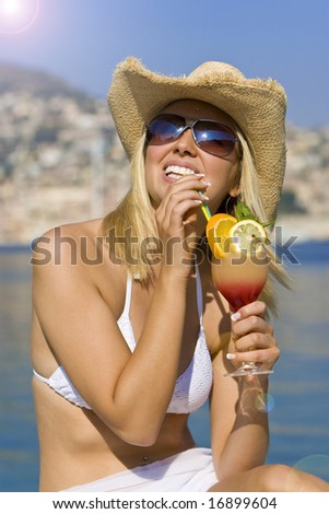 A beautiful and happy young blond woman sitting by the sea drinking a cocktail