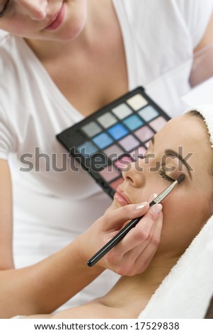 A beautiful young woman having the finishing touches applied to her make up by a beautician