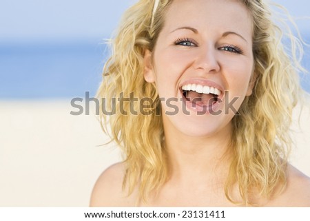 A sexy and beautiful young blond woman gives a big natural laugh while at the beach