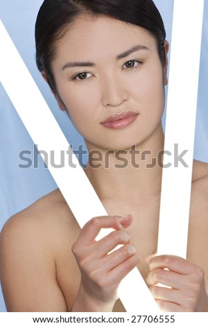 A stunningly beautiful young Japanese woman holding glowing fluorescent tubes in a fresh blue studio setting