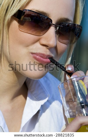 A beautiful young blond woman drinking a cool drink through a drinking straw on a hot summer day