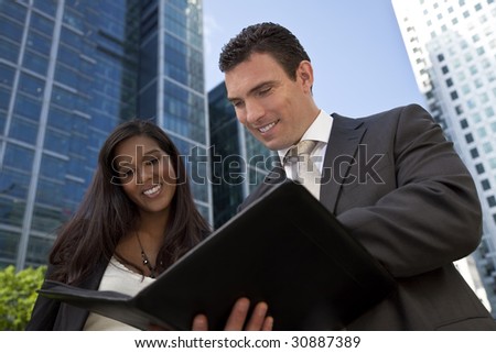 A smiling businesswoman and her male colleague taking part in a happy business meeting outside in a modern city environment