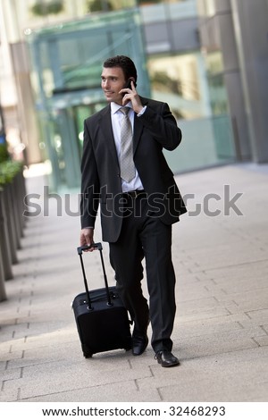 Successful businessman traveling with his suitcase and talking on his cell phone. Shot on location in a city or airport setting.