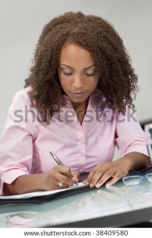 A beautiful mixed race African American girl, student or businesswoman sitting at a desk and writing.