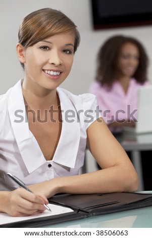 A beautiful young Chinese oriental Asian woman working in an office with her African American colleague out of focus behind her.