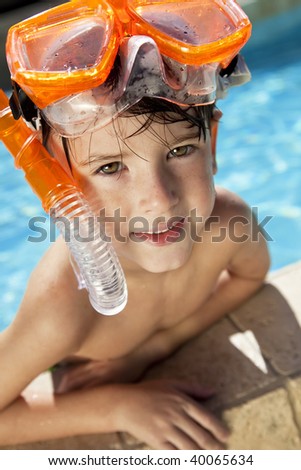 A happy young boy relaxing on the side of a swimming pool wearing orange goggles and snorkel