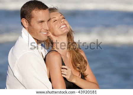 A young man and woman embracing and laughing as a happy romantic couple on a beach