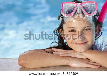 A cute happy young girl child relaxing on the side of a swimming pool wearing pink goggles and snorkel