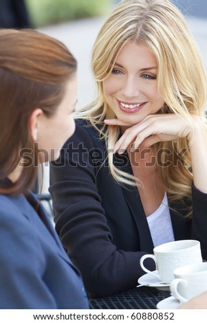 Two beautiful and sophisticated young women friends having coffee around a modern outdoor city cafe table