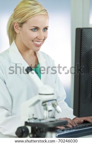 A smiling female medical or scientific researcher or woman doctor using a computer in a laboratory with microscope and other equipment in the foreground.