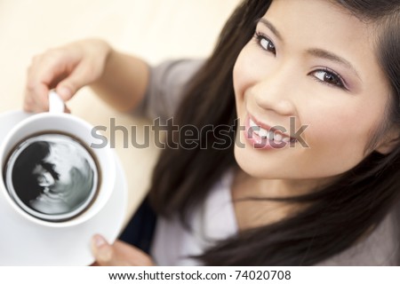A beautiful young Chinese Asian Oriental woman with a wonderful toothy smile drinking tea or coffee from a white cup and saucer