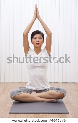 A beautiful young Chinese Asian Oriental woman sitting cross legged in a yoga position at a gym