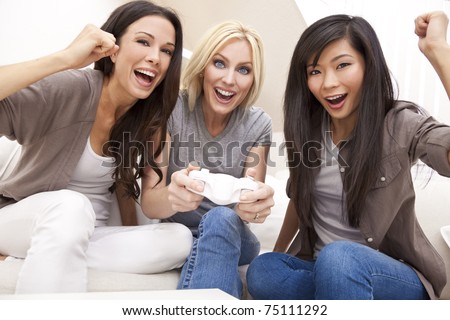 Three beautiful interracial young women friends at home having fun playing video games together and laughing