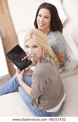 Overhead photograph of two beautiful young women at home sitting on sofa or settee using a tablet PC computer and smiling