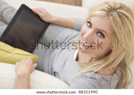 Overhead photograph of a beautiful young women at home sitting on sofa or settee using a tablet PC computer and smiling