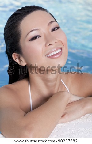 A beautiful sexy young Chinese Asian Oriental woman wearing a bikini and relaxing on the side of a swimming pool.