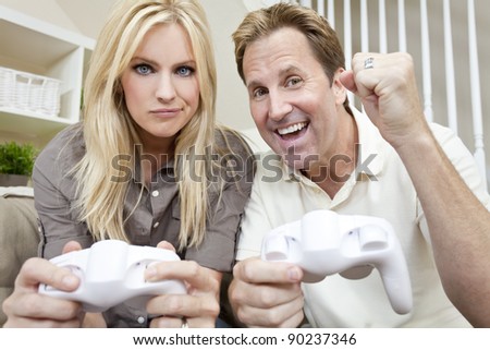 Young married couple, man and woman, having fun playing video console games together. The man has just beaten the woman, he is celebrating, she is unhappy.