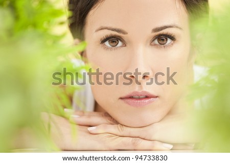 Health spa nature concept studio portrait of a beautiful young woman or girl resting on her hands smiling through natural green leaves