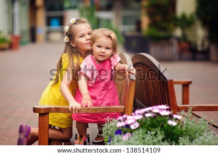 Two lovely little sisters outdoors in city at beautiful summer day hug and smile