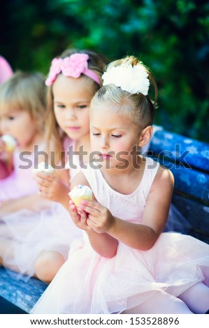 group of little girls in princess costumes celebrate birthday and eat cupcakes