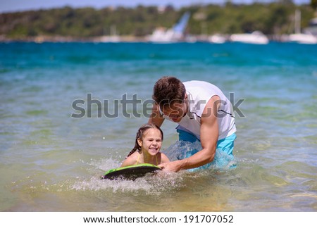 Father learning kid to swim with a board at sea