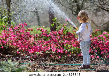 Cute little girl watering flowers in the summer garden