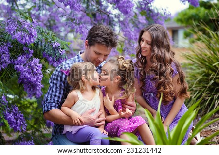 Young beautiful family of mother, father and two little daughters in jacaranda blossom garden