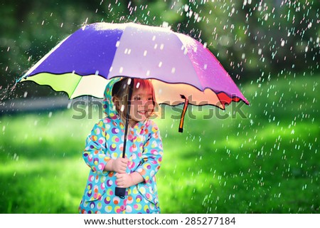 Funny cute toddler girl wearing waterproof coat with colorful umbrella playing in the garden by rainy and sunny day