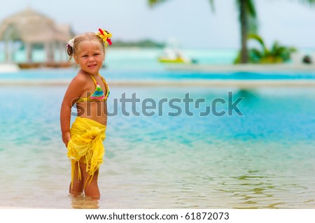 Toddler pretty girl in bikini standing on tropical beach