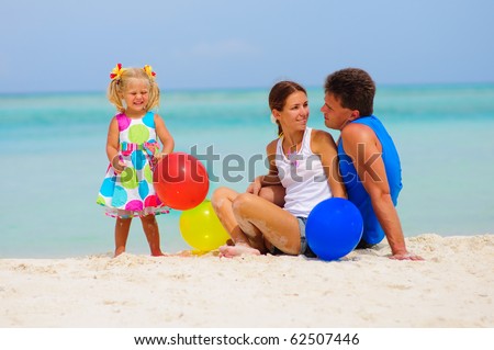 happy young family of three have a party with colorful balloons on tropical beach