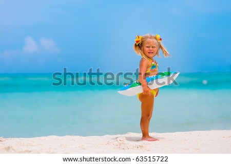 Toddler pretty girl dressed in bikini standing on tropical beach with inflatable circle