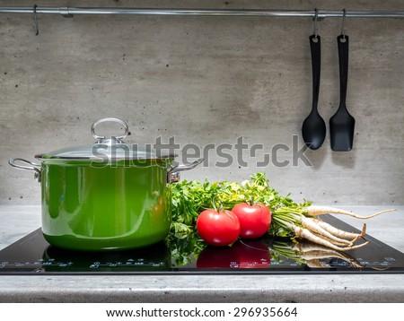 Green enamel stewpot with parsley and two tomatoes on black induction cooker