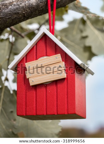 Wooden red birdhouse hanging on tree branch with entry hole covered with planks