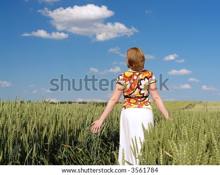 Woman wearing flowered blouse and white skirt strolling through wheat crop in dreamy mood skimming delicately corn ears with her palms