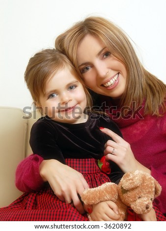Young mom and her cute little daughter holding teddy-bear posing happily sitting on sofa