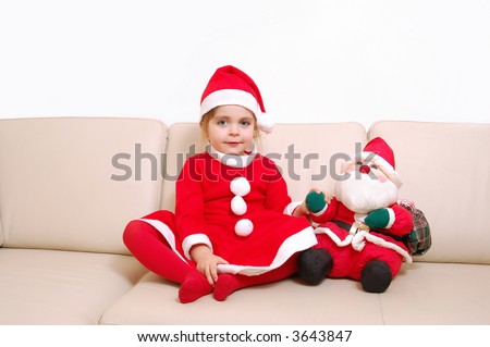 Little cute girl dressed in santa clause costume posing on sofa with santa clause doll