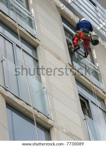 Window washer washing office building windows hanging outside the building on ropes