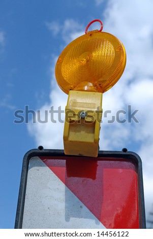 Closeup of red and white striped road warning post with orange beacon over blue sky
