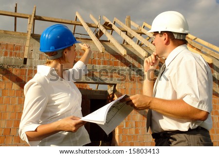 Female investor discussing building plans with the site manager against unfinished brick house with wooden roof structure
